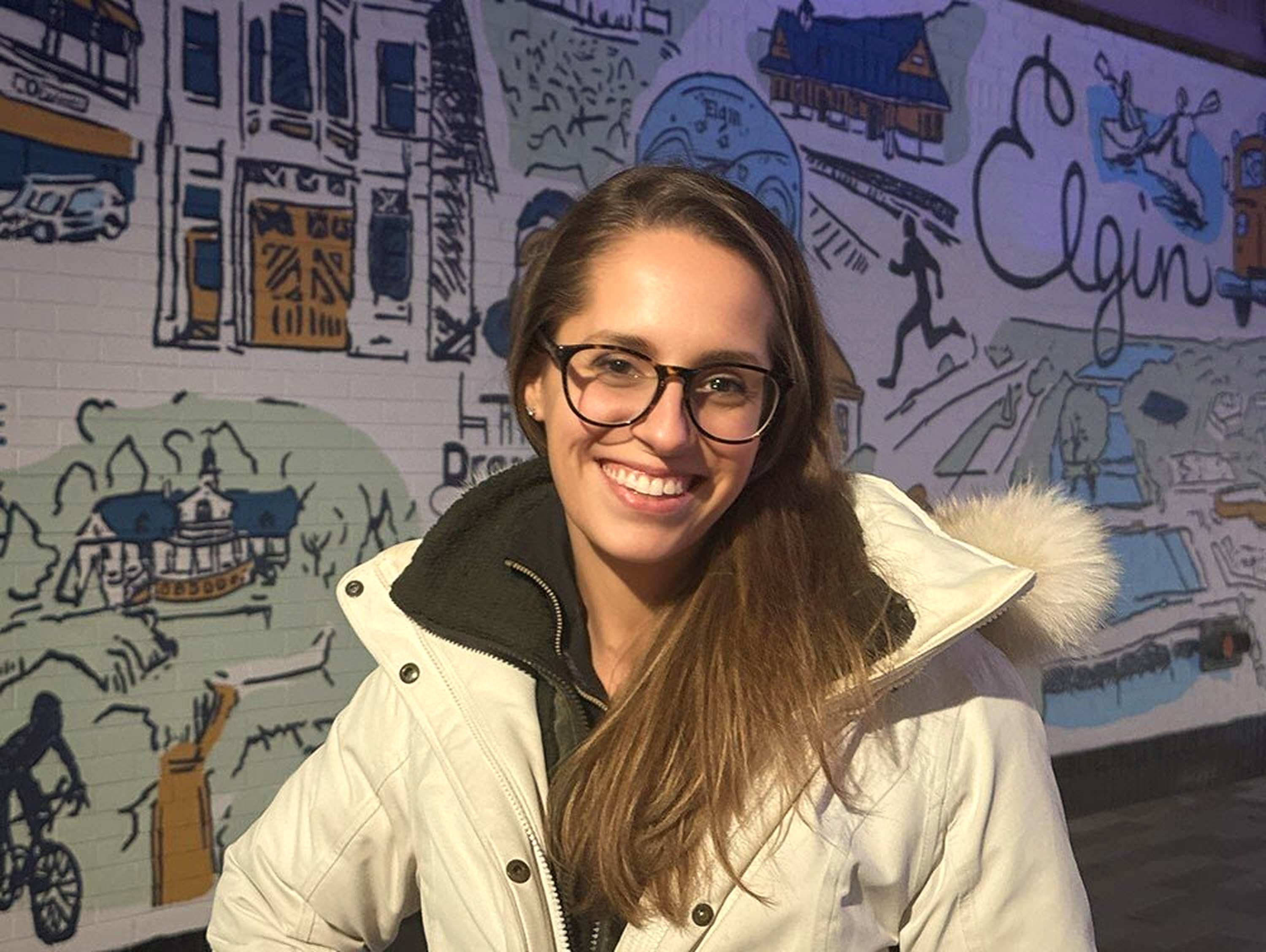 Artist Ashley Ann standing in front of the Elgin mural created from her community mug artwork